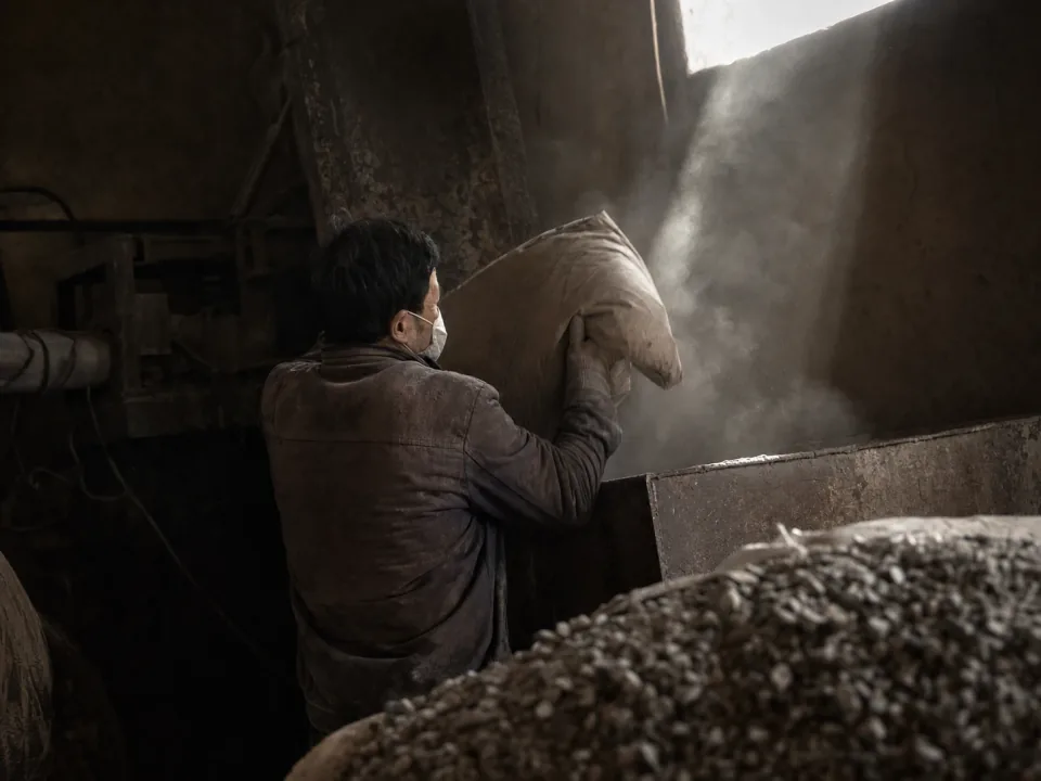 Operator loading bagged cement beside a batching plant hopper