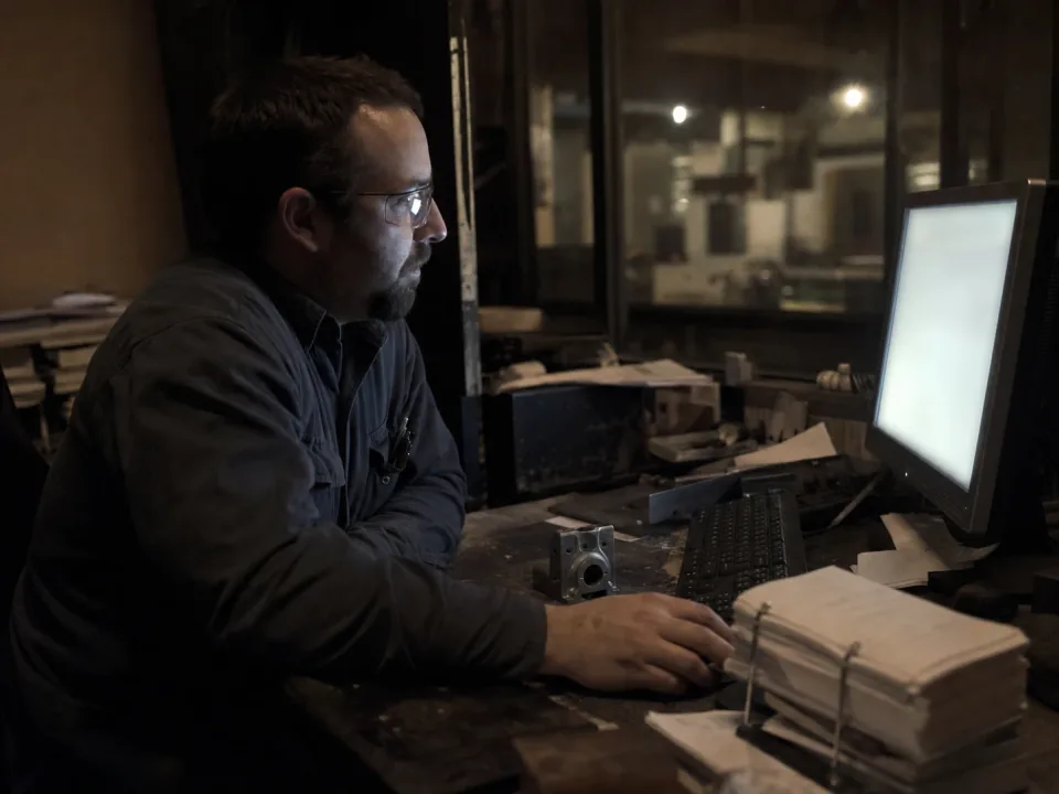 Quality engineer at a desk assembling a cert pack beside the shop floor