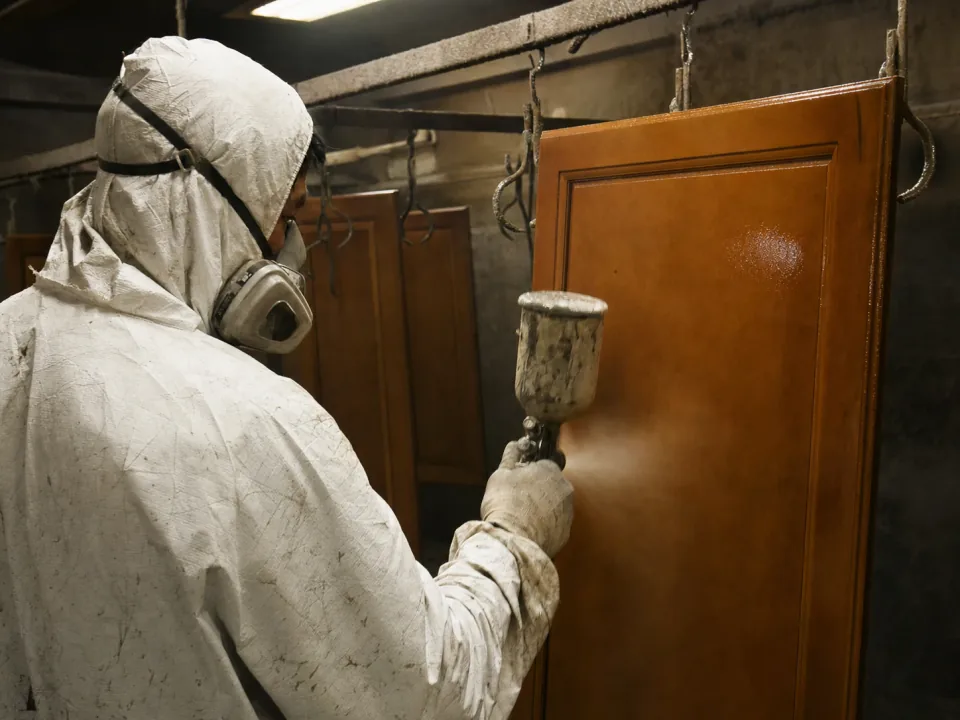 Sprayer lacquering a cabinet door in a finishing booth
