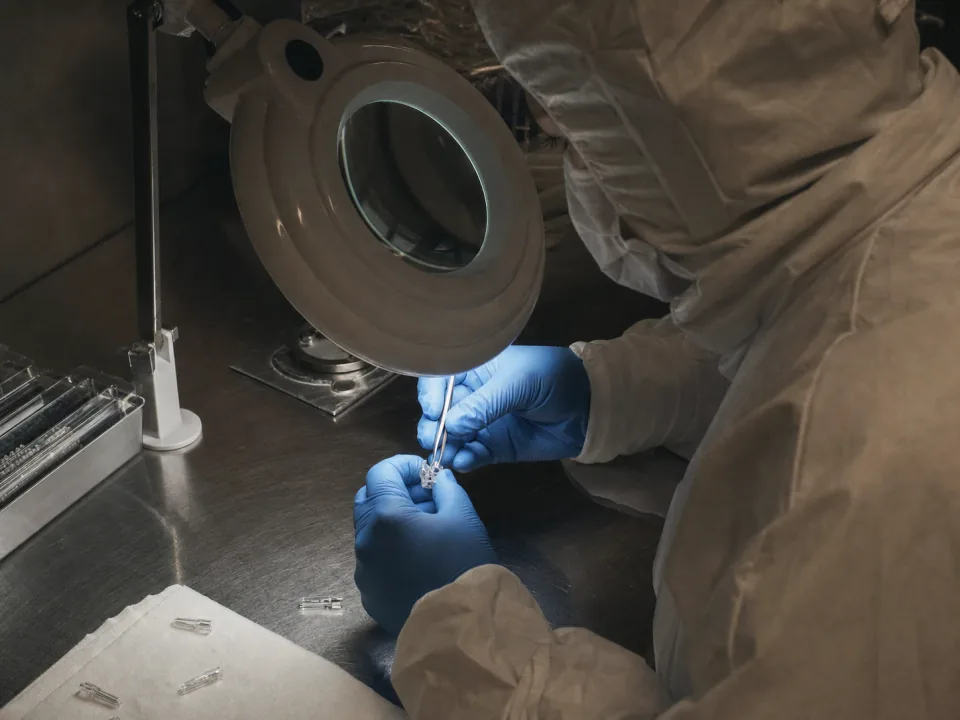 Gowned operator assembling a small surgical device at a cleanroom bench