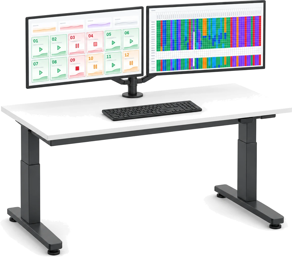 A height-adjustable desk with two monitors: a live asset board of running, paused and stopped machines, and an hour-by-hour status heatmap of every asset.